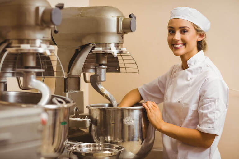 Smiling woman in bakery using dough kneading machine
