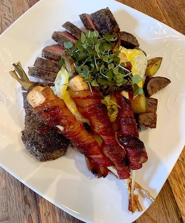 Sous vide reverse-seared NY Strip with roasted purple and white potatoes, hollandaise, over easy egg, maple-glazed bacon wrapped parsnips and red mustard micro greens