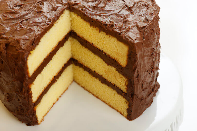 a three layer white cake covered in chocolate frosting on a white plate