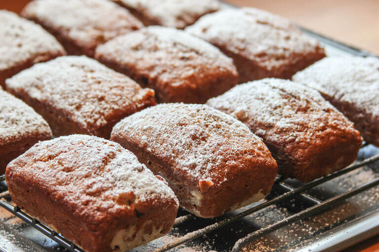 loaves of walnut banana bread dusted with powdered sugar sit on cooling racks