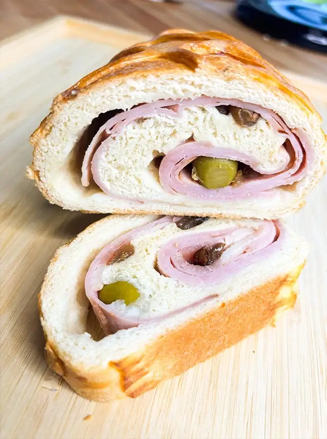 Sliced pan de jamón showing rolled ham, green olives, and raisins inside golden baked bread.