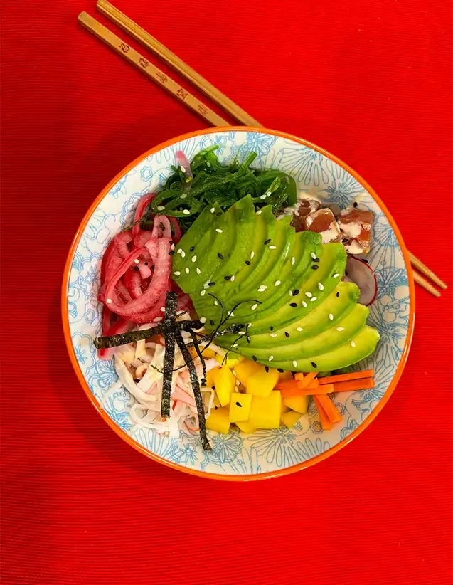 Colorful poke bowl with avocado, pickled onion, seaweed, tuna, and veggies on a red background