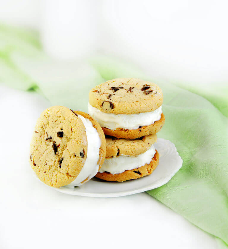 three chocolate chip cookie ice cream sandwiches sitting on a white plate