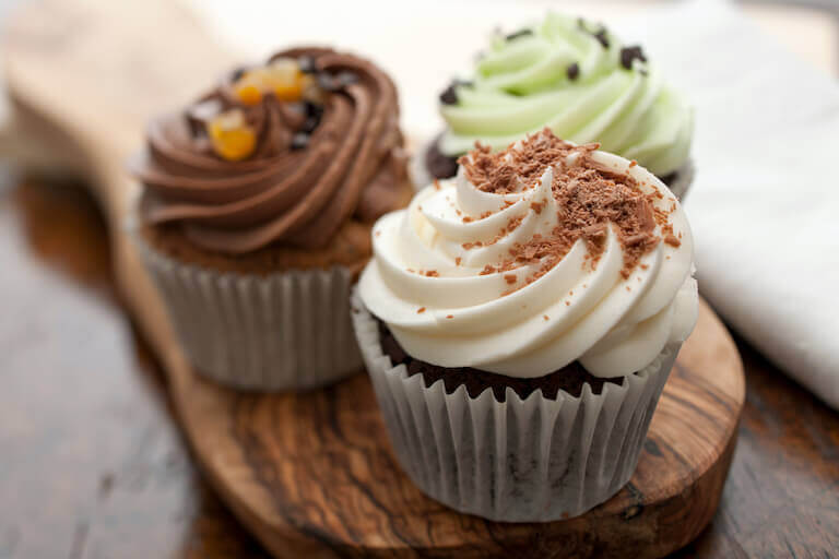 three chocolate cupcakes sitting on a wood plate