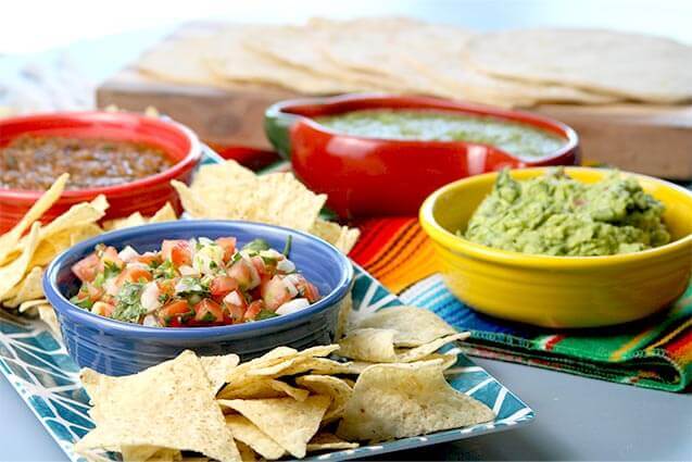 various salsas guacamole in multi-color dishes with chips