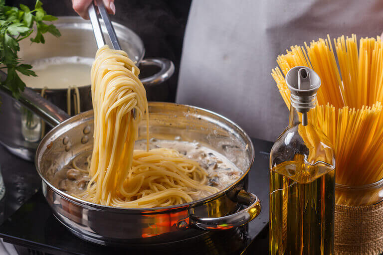 young woman in a gray apron preparing spaghetti pasta next to bottle of olive oil