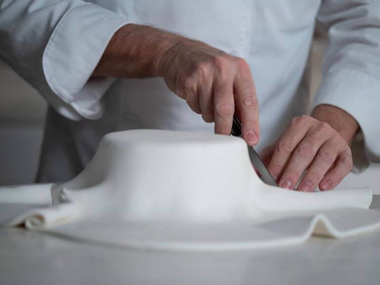 Cake decorator applying white fondant to a cake