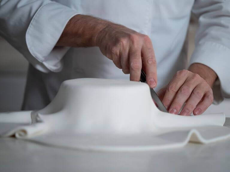 Chef cutting away excess white fondant draped over a layer of cake.