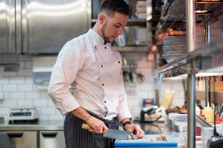 Chef cutting shrimp with a large knife on a cutting board