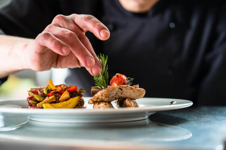 Chef finishing and garnishing a dish with pork meat and vegetables