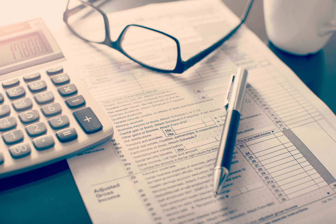 Income tax return form sitting under a calculator, pen, and glasses