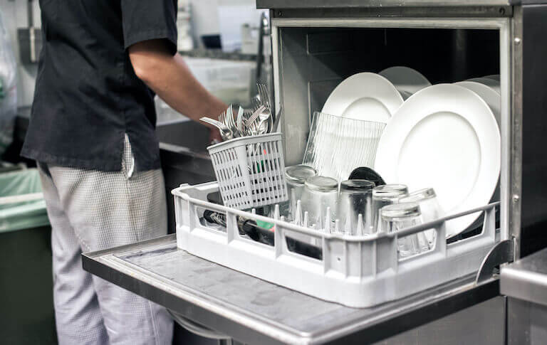 Kitchen employee washing dishes next to an open dishwasher