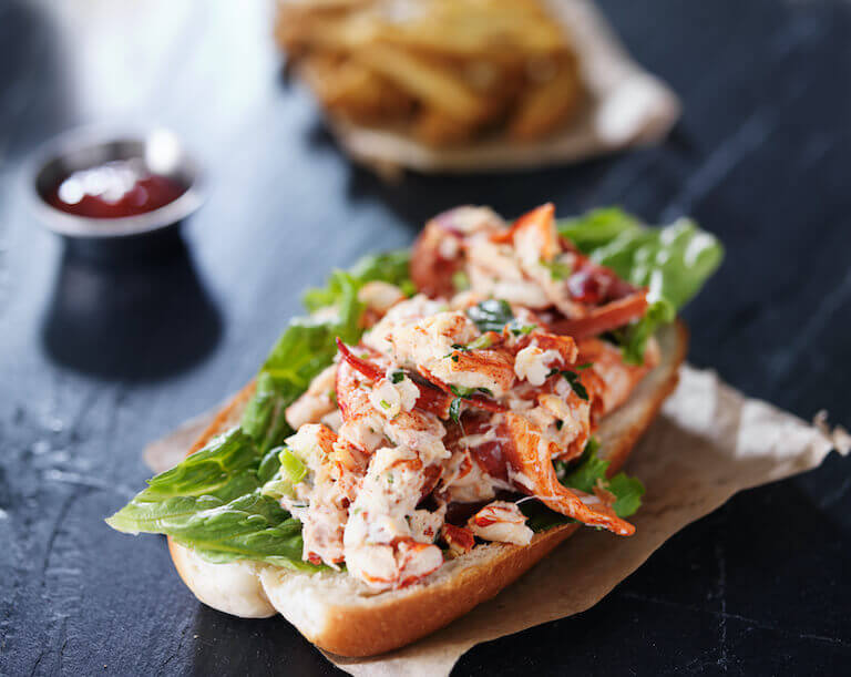 Lobster roll with lettuce on a black slate surface