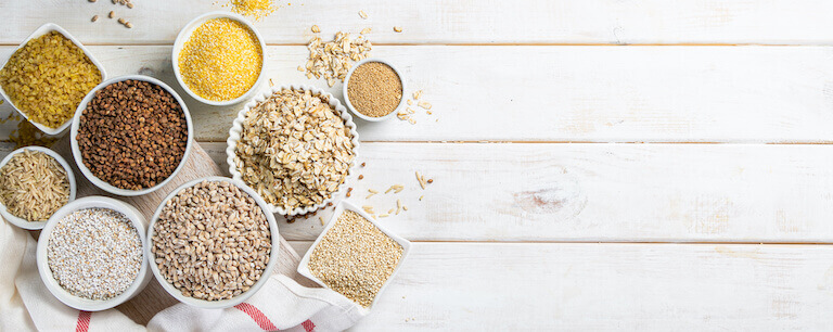 Rice, oats, quinoa, and other whole grains in white bowls on a wooden table
