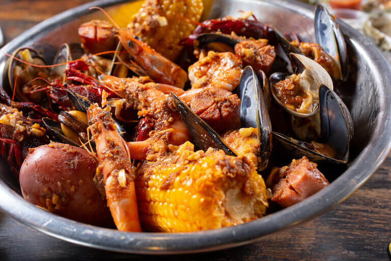 Silver bowl filled with corn, mussels, crawfish, shrimp, clams, and corn