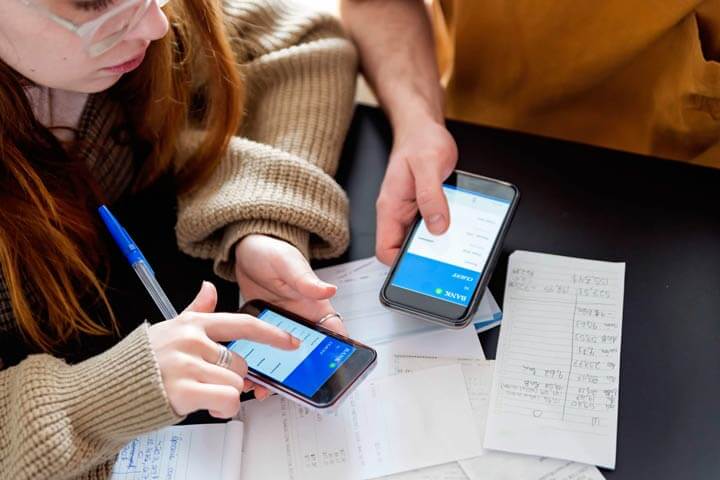 Two young adults looking at a banking app on their phones while they calculate bills