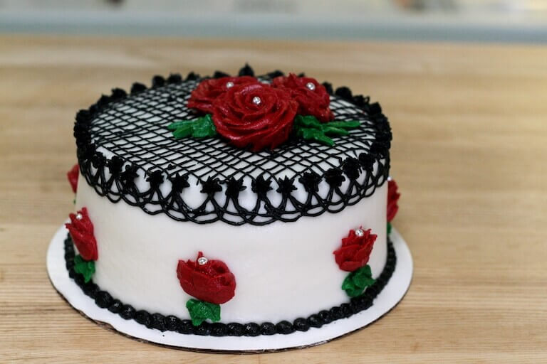 White cake decorated with black piping and red roses