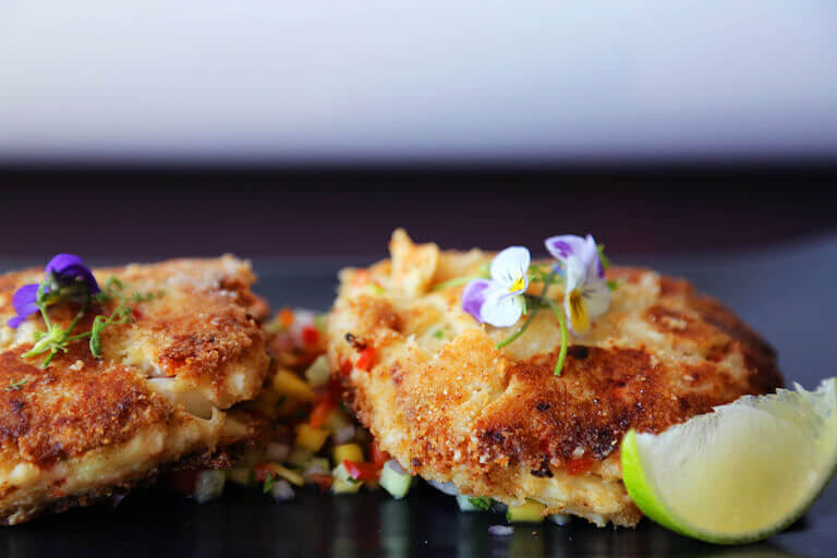 crab cakes garnished with a purple flower and lime