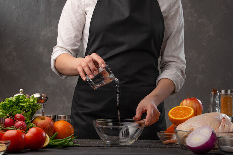 A chef pours water into a glass bowl