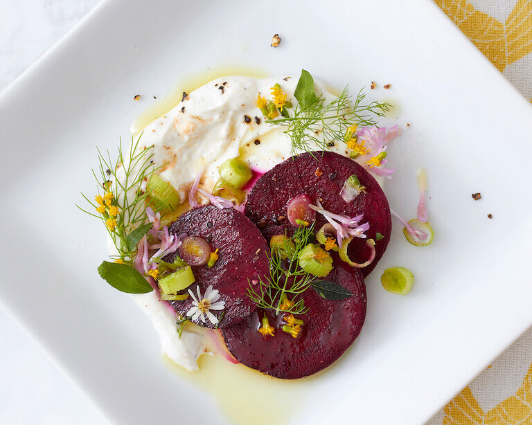 An artfully plated beet salad dish on a white square plate