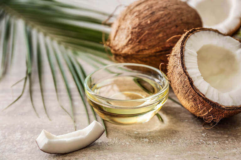 Bowl with coconut oil and coconuts on table