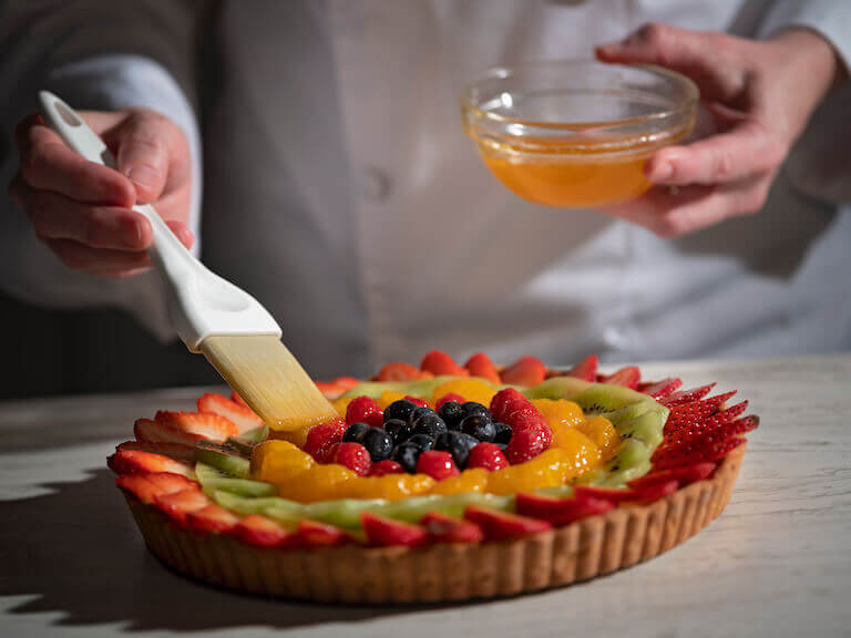 Brushing apricot glaze on a fruit pie with strawberries, kiwis