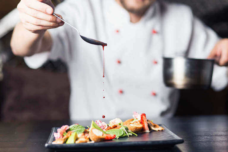 Chef using spoon to pour red sauce over a plate