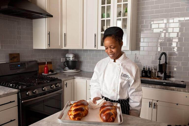 Escoffier online student smiling and holding a baking sheet with finished bread.