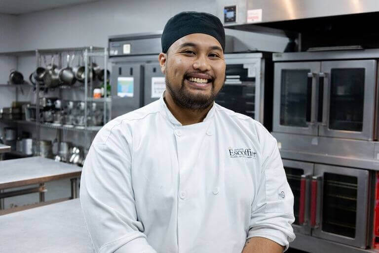 Escoffier student in uniform smiling for a photo in a kitchen