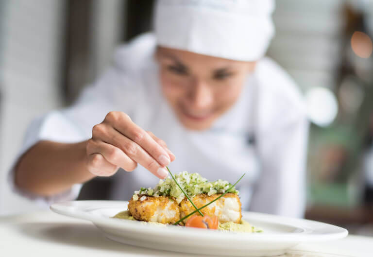 Female chef plating and garnishing a breaded chicken dish