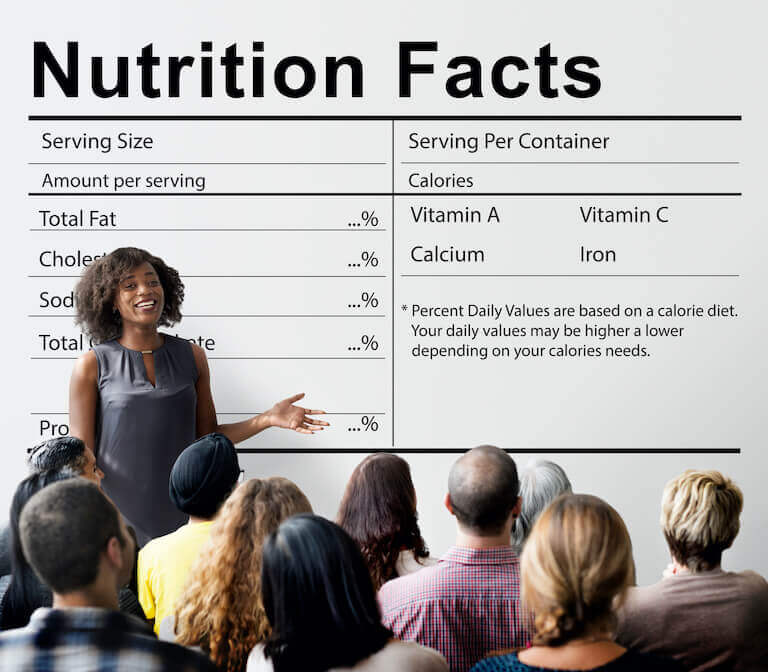 Health coach speaking to a class while standing in front a board with nutrition facts