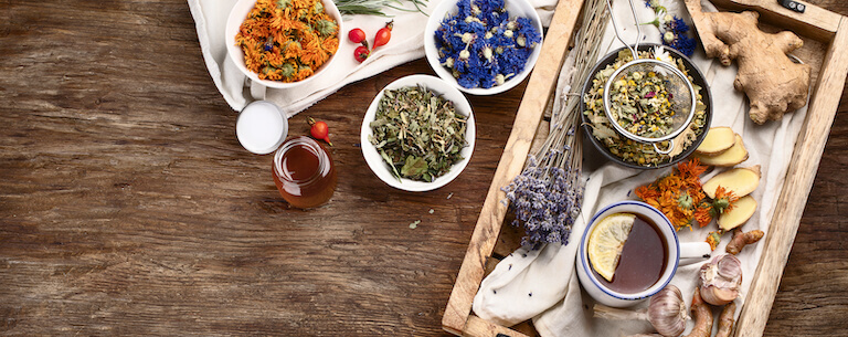 Herbs, flowers, tea, and ginger sit on a wooden table.