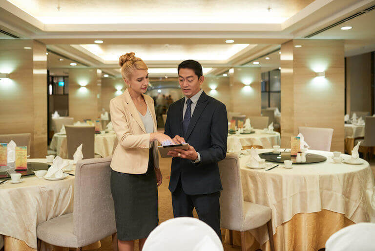 Male and female managers discussing upcoming banquet while looking at tablet