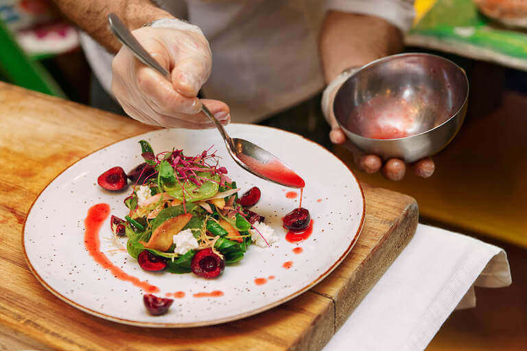 Plating green salad on white plate with red dressing