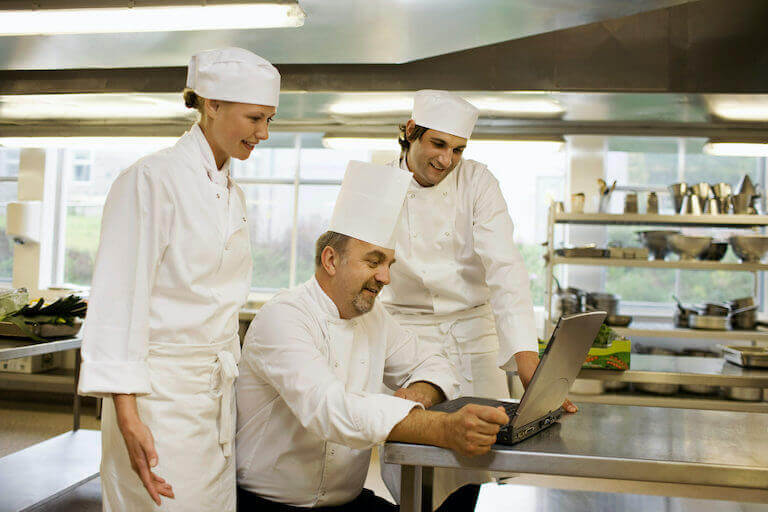Three chefs looking at a laptop