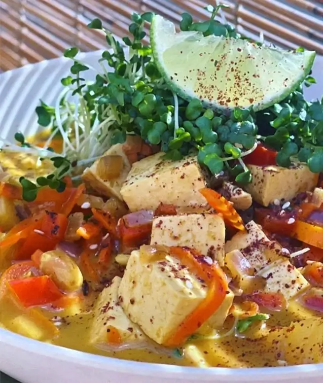 Tofu curry bowl with carrots, bell peppers, sprouts, and a lime wedge in a creamy golden sauce