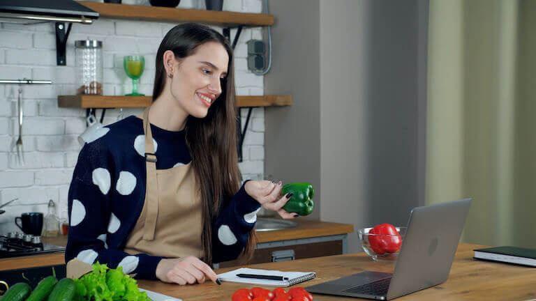 Woman teaching on her computer while holding a green bell pepper