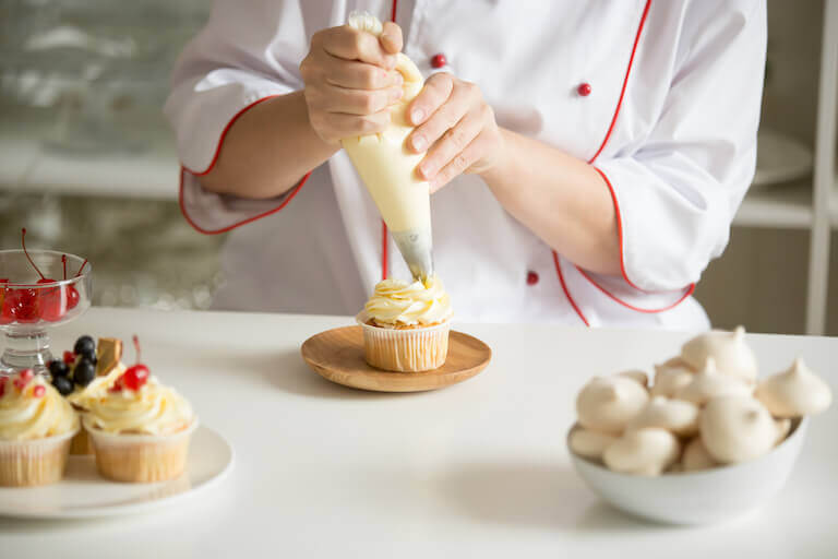 Baker frosting a cupcake in the kitchen