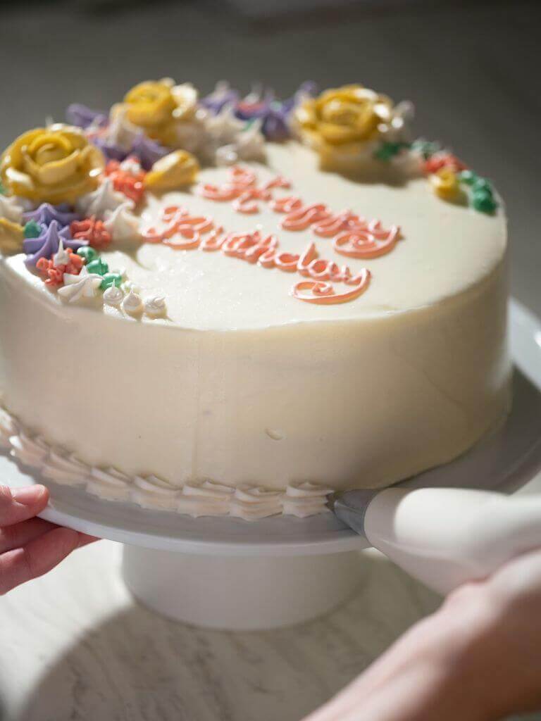 Cake decorator piping a shell border on to a birthday cake