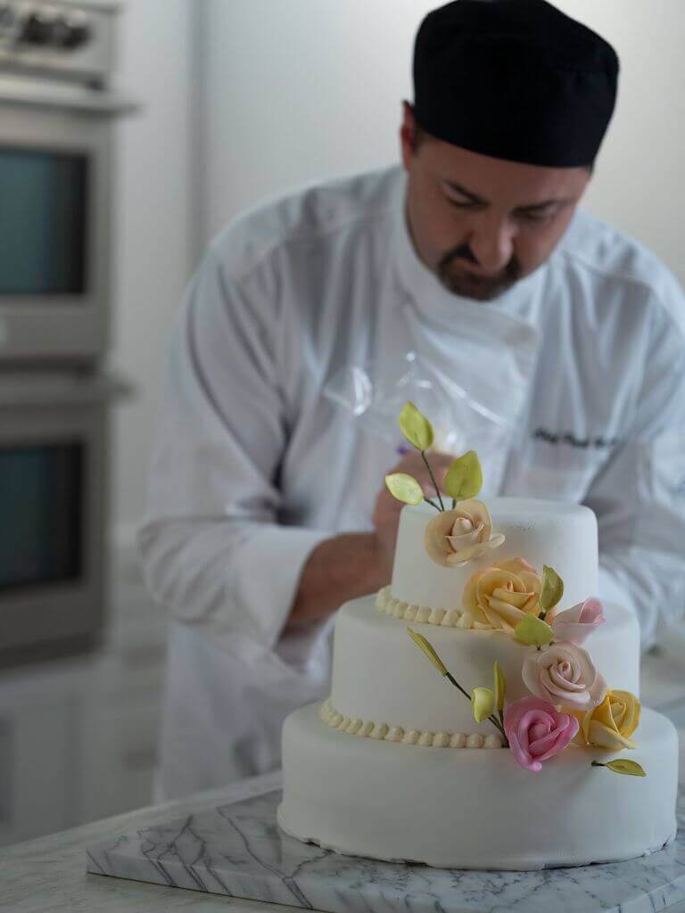 Chef decorating a tiered cake with roses on it