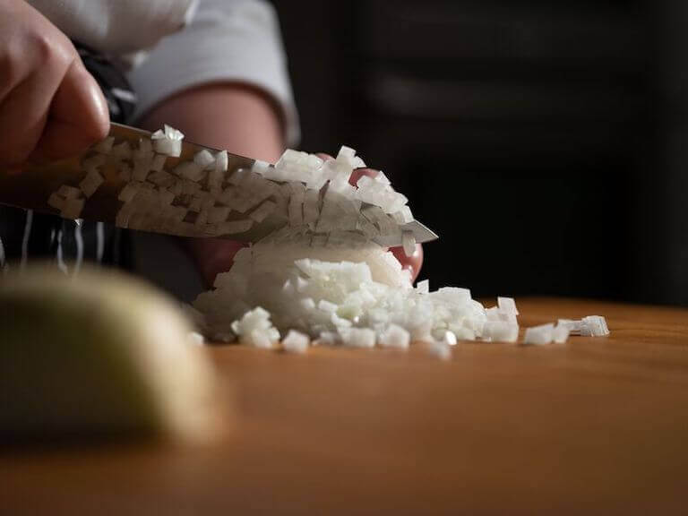 Closeup view of a pair of hands dicing an onion.