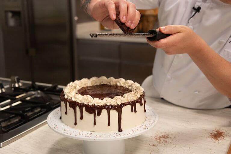 Chef grating chocolate on a vanilla cake