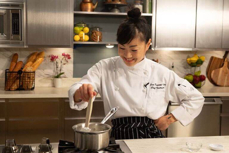 Chef instructor stirring sauce in a metal pot on the stove