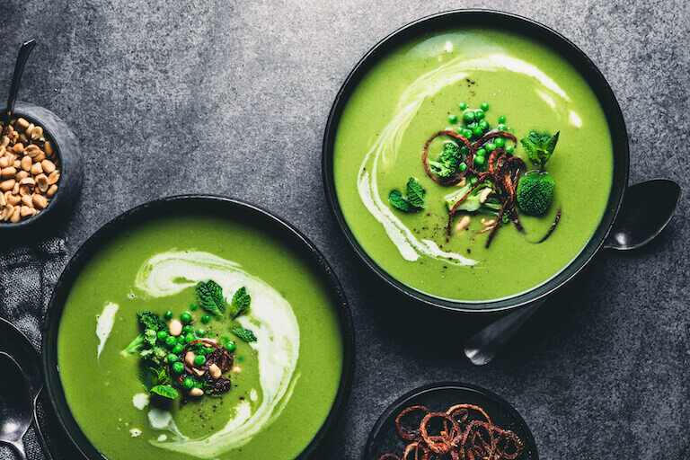 Green plant based soup in a black bowl with broccoli and peas