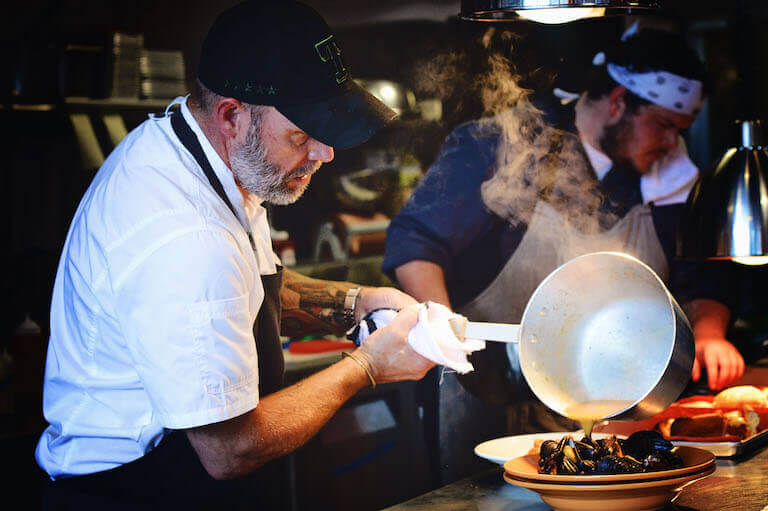 Lance McWhorter pouring broth over mussels dish