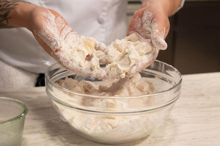 Pastry chef kneading pie dough in a glass bowl