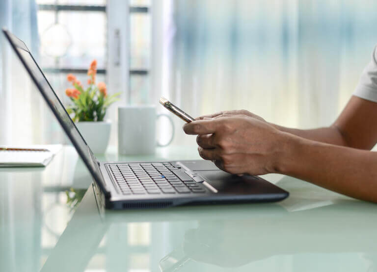 Person using a laptop while also holding their phone