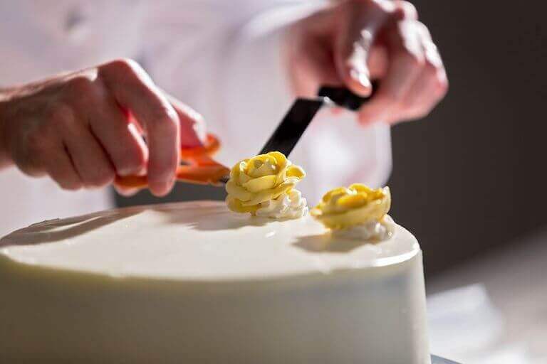 Cake decorator placing two yellow roses on a cake