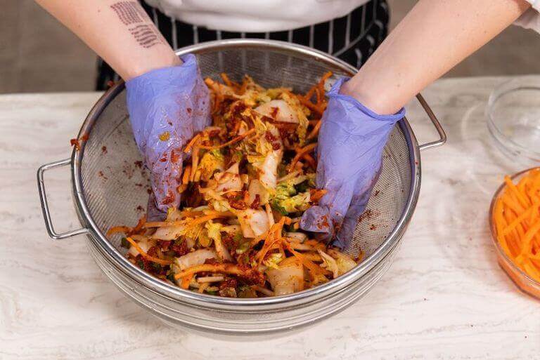 Chef mixing kimchi in a glass bowl