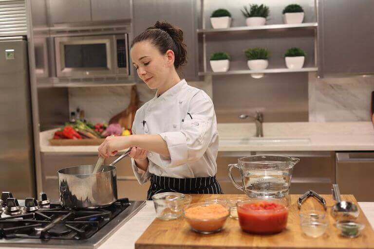 Chef stirring a pot on the stove next to ingredients in glass bowls
